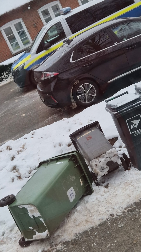 Drei Mülltonnen hinter einem Schneewall am Straßenrand, zwei davon liegen umgekippt auf dem Gehweg.