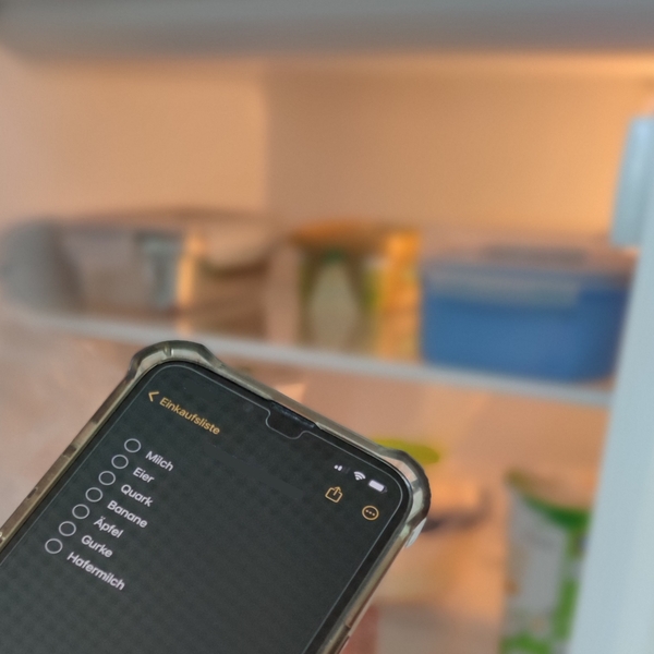 Einkaufsliste auf Handydisplay vor geöffnetem Kühlschrank