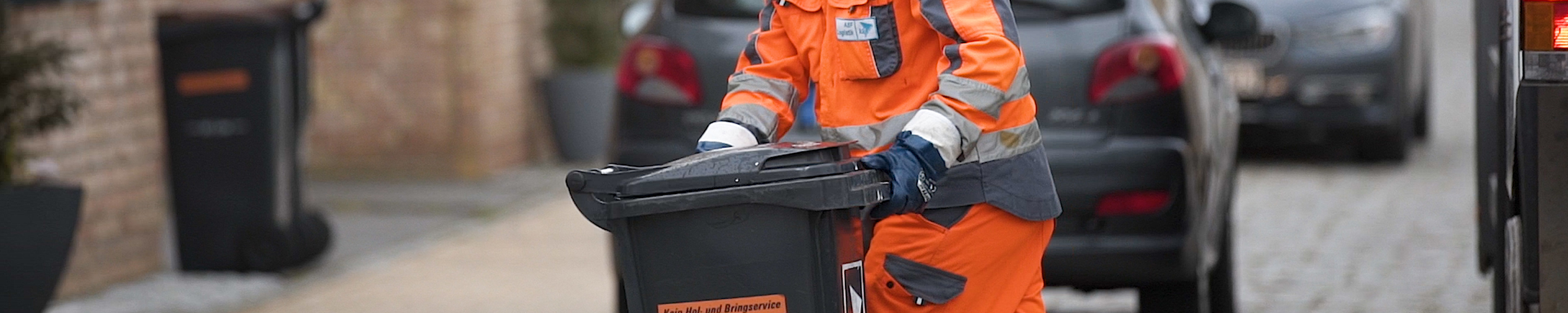 Müllwerker schiebt eine Tonne zum Fahrzeug